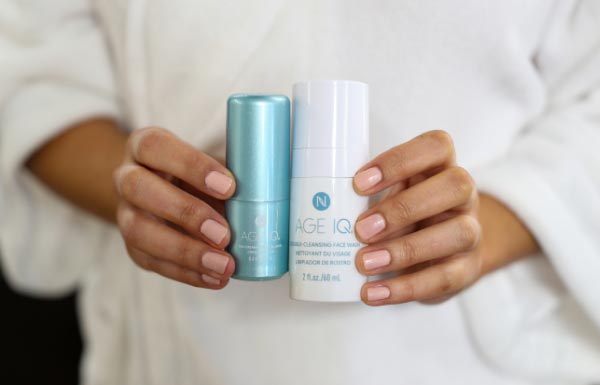 Lifestyle shot of a woman wearing a robe holding the Age IQ Travel Minis Cleanser & Day Cream Combo bottles in her hands.