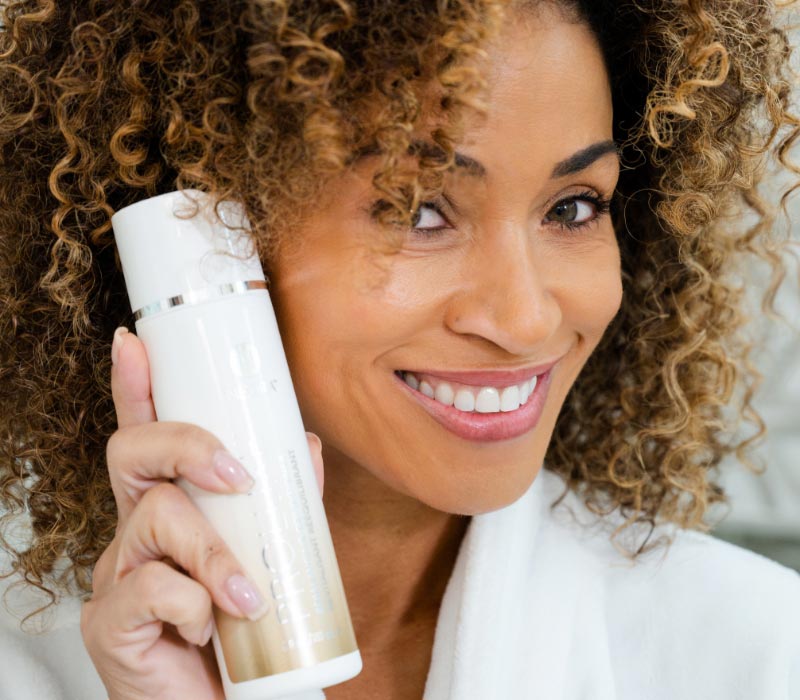 Woman holding Neora’s professional-grade, nourishing ProLuxe Rebalancing Conditioner and smiling